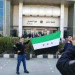 طلاب يرفعون العلم السوري الجديد أمام كلية الحقوق جامعة دمشق (الجزيرة)