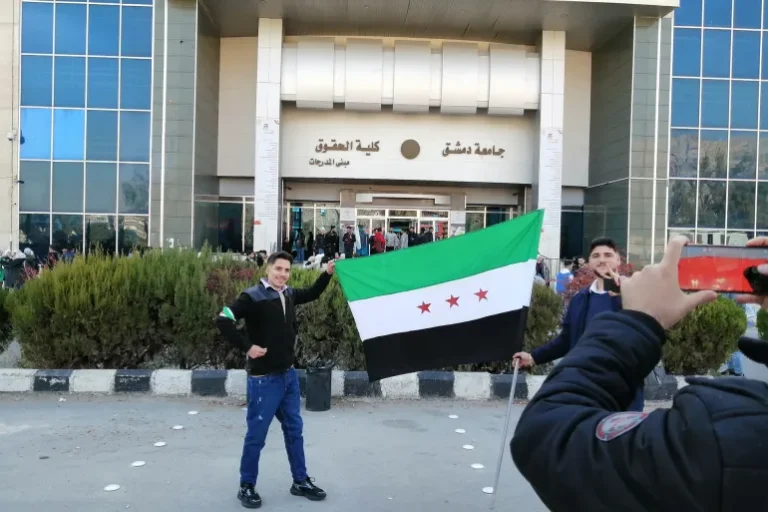 طلاب يرفعون العلم السوري الجديد أمام كلية الحقوق جامعة دمشق (الجزيرة)