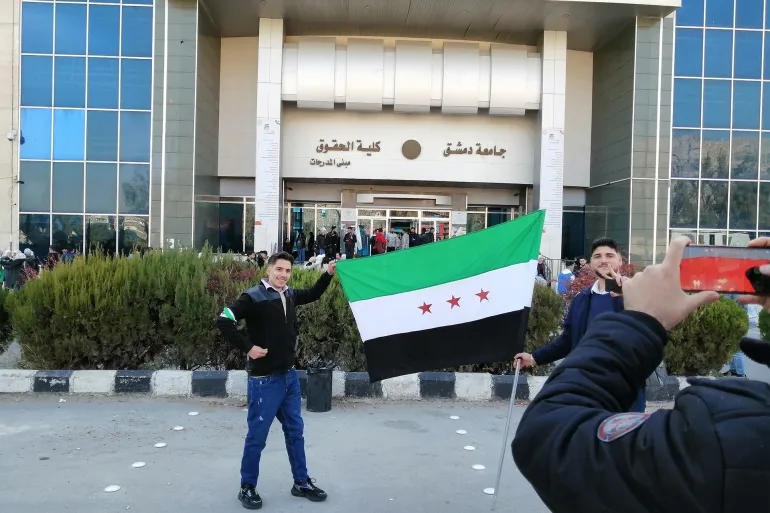 طلاب يرفعون العلم السوري الجديد أمام كلية الحقوق جامعة دمشق (الجزيرة)
