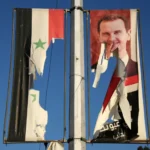 لوحة إعلانية تحمل صورة الأسد وعلم سوريا السابق بعد أن مزقها مناهضون له في حلب (الفرنسية)