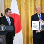 الرئيس الأميركي (يمين) يرحب برئيس الوزراء الياباني ويحمل صورة للقائهما في المكتب البيضاوي (الفرنسية)