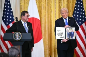 الرئيس الأميركي (يمين) يرحب برئيس الوزراء الياباني ويحمل صورة للقائهما في المكتب البيضاوي (الفرنسية)
