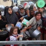 فلسطينيون مجوّعون ينتظرون وجبات غذائية من مؤسسات إغاثة في مخيم النصيرات (الفرنسية)