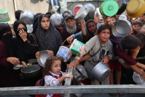 فلسطينيون مجوّعون ينتظرون وجبات غذائية من مؤسسات إغاثة في مخيم النصيرات (الفرنسية)