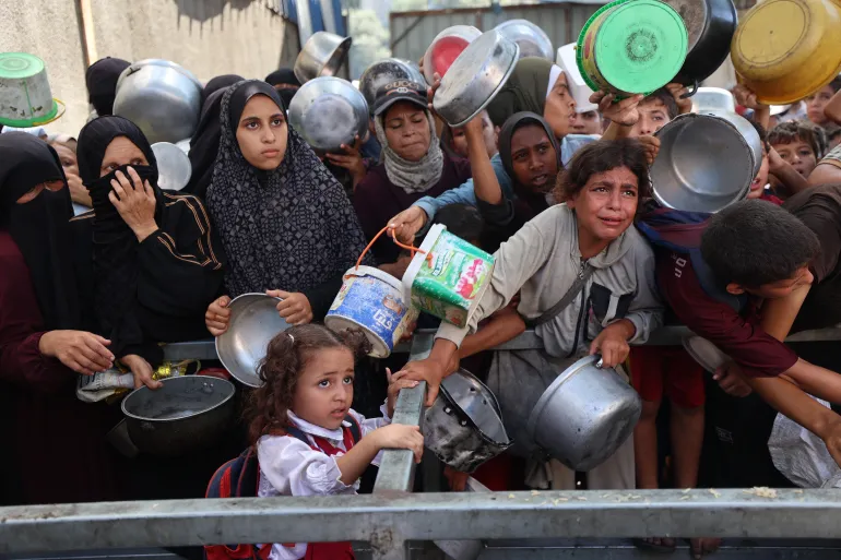 فلسطينيون مجوّعون ينتظرون وجبات غذائية من مؤسسات إغاثة في مخيم النصيرات (الفرنسية)